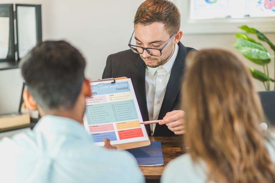 A professional consultant or inspector with short, light brown hair, wearing black-rimmed glasses, a dark suit jacket, and a white shirt, is seated at a desk holding a clipboard with a detailed home i